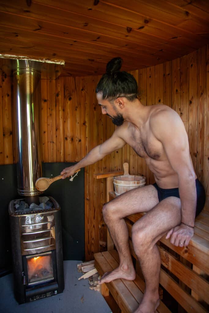 Sauna finlandese con stufa Harvia a legna con fuoco a vista e il mestolo d'acqua versato sulle pietre roventi nel il rito del Löyly
